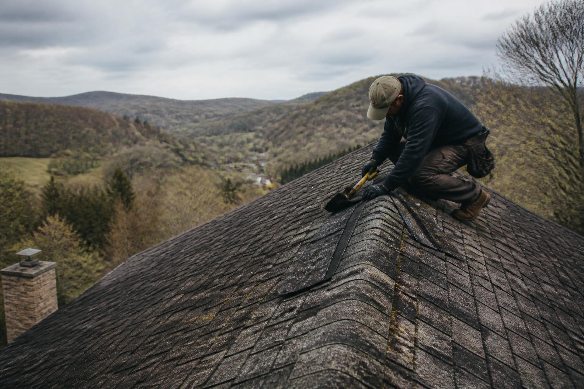 Contractor repairing an asphalt shingle roof above a West Virginia valley
